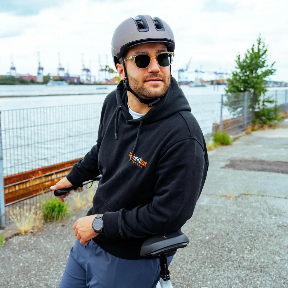 Mann sitzt auf Fahrrad und schaut zur Kamera | Rad und Tat